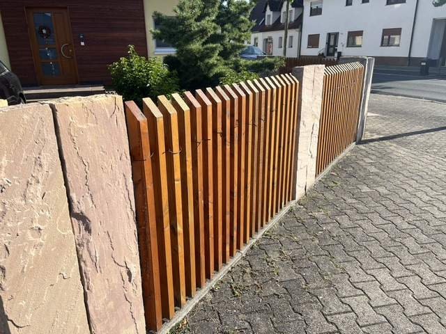 Sichtschutzzaun aus senkrechten Holzlatten zwischen Sandsteinstelen an einer Grundstücksgrenze