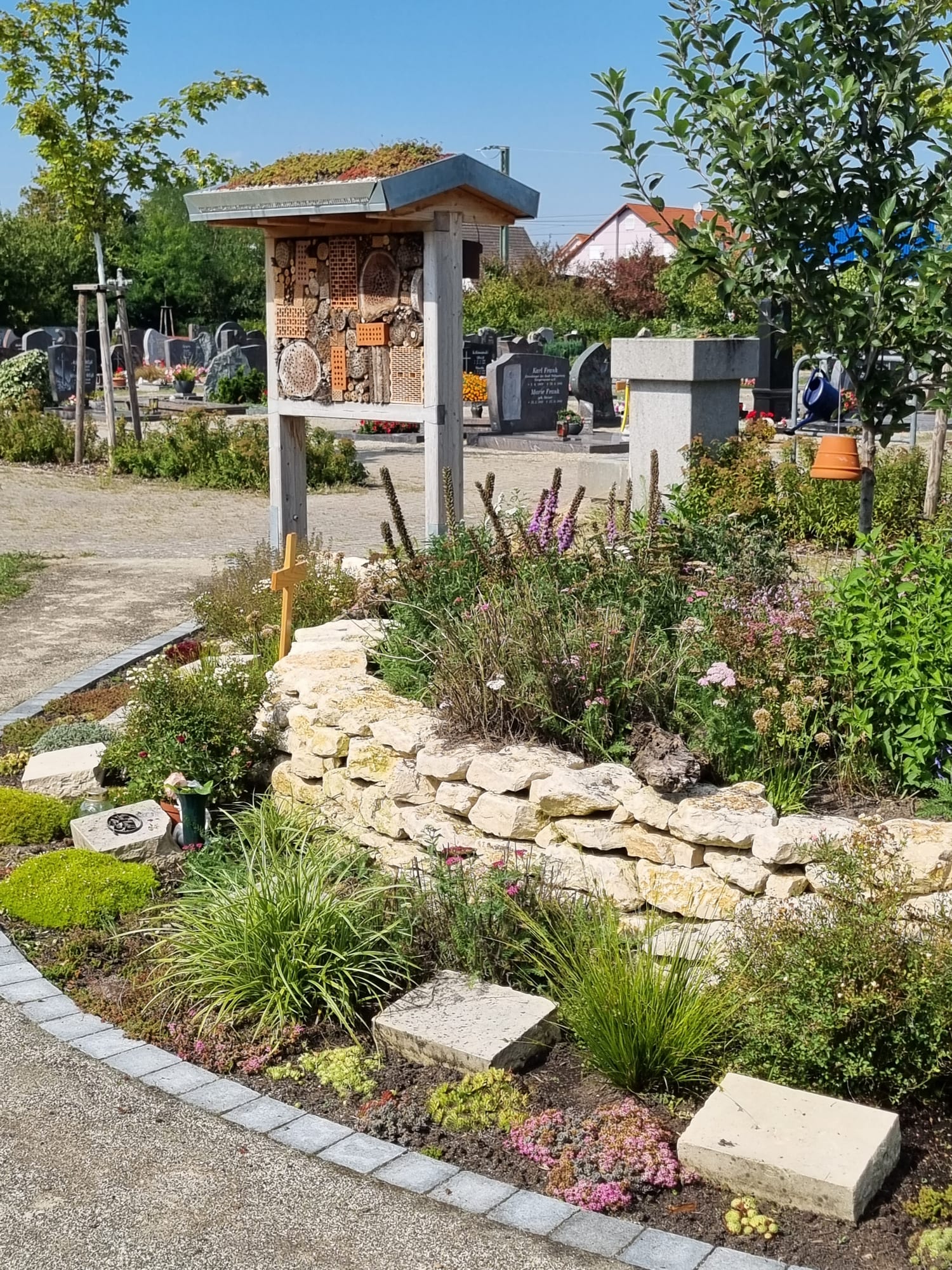 Naturnah bepflanztes Gemeinschaftsgrabfeld mit Trockenmauer aus Naturstein, Stauden und Insektenhotel