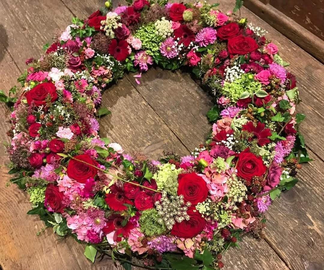 Herzförmiges Trauergesteck aus roten und orangefarbenen Blüten
