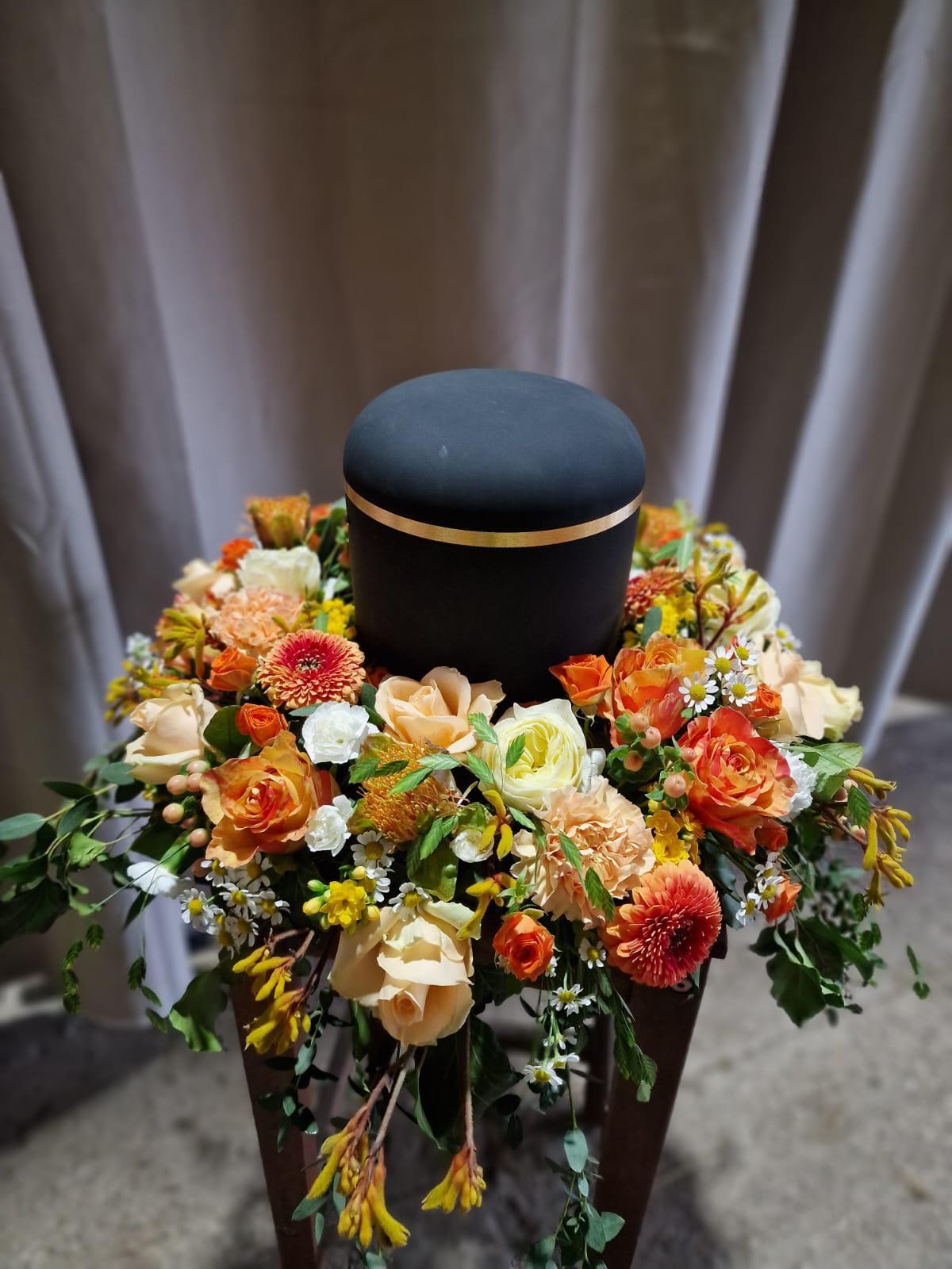 Schwarze Urne mit umlaufendem Blumenkranz in Orange- und Gelbtönen