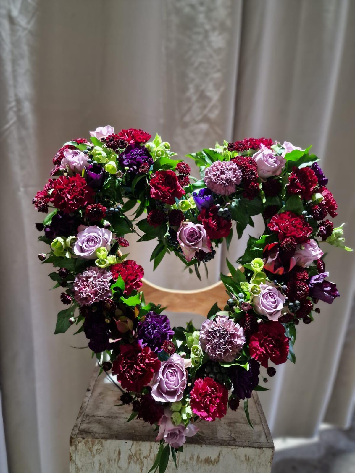 Offenes Herzgesteck aus lilafarbenen und roten Nelken und Rosen